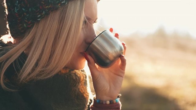 The woman is opening a flask and drinking coffee from a cap. The girlfriend is enjoying the weekend and time with her boyfriend in nature.