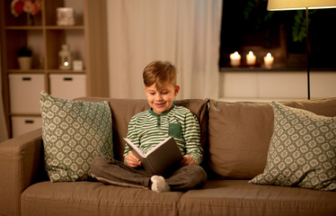 childhood and people concept - happy little boy reading book at home