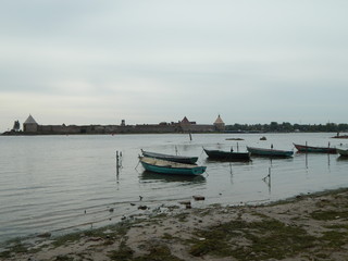 On the calm water of the lake there are several boats, in the distance the fortress walls - a beautiful summer landscape.