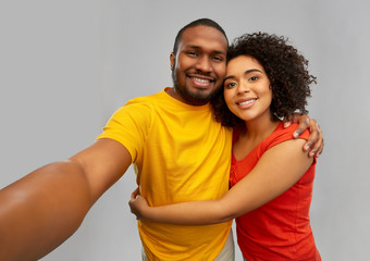technology and people concept - happy smiling african american couple taking selfie over grey...