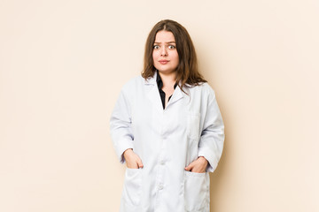 Young doctor woman shrugs shoulders and open eyes confused.