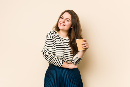 Young curvy woman holding a coffee laughing and having fun.