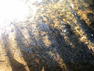 Ripples in the river flow through the rocks, colorful in the summer in bright sunlight, have background of the shiny pebbles, at the bottom of river In a abstract, form of pebbles below water surface.