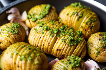 Hasselbeck potatoes with green basil pesto and garlic. Served on pan. 