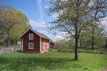 Fototapeta na wymiar Countryside living idyll - Rural Swedish idyllic landscape in springtime - Red painted houses and plowed fields in the travel destination Asens By in Smaland Sweden. 