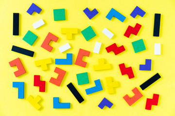 Colorful wooden blocks of different shapes puzzles on yellow background. Natural, eco-friendly toys. Creative, logical thinking concept. Background with geometric shapes wooden blocks.