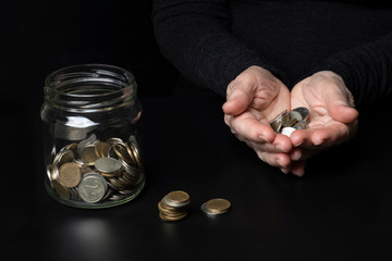 The concept of poverty. The hands of an elderly woman holding coins and jar of coins on dark...