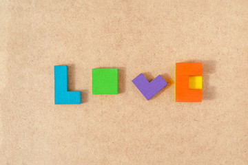 Word LOVE made from colorful wooden bricks toys on kraft cardboard background. Parents love and kids game concept. Top view, flat lay.