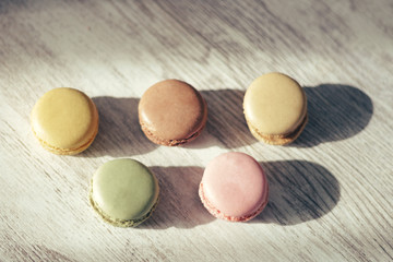 Macaroons illuminated by sun rays casting their shadow, on a gray handmade wooden background, selective focus