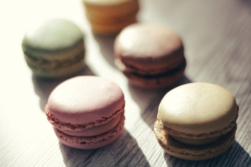 Macaroons illuminated by sun rays casting their shadow, on a gray handmade wooden background, selective focus, macro view