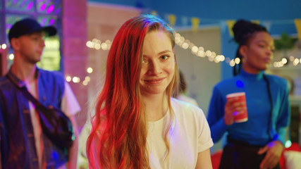 Beautiful young girl with charming smile looking at camera staying with best friends celebrating disco party reunion together. Communication and friendship concept.