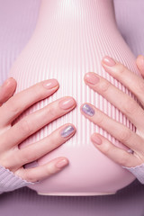 Beautiful female hands holding pink vase on the pale violet background. Manicure with pink color nail polish with shiny design. Copy space