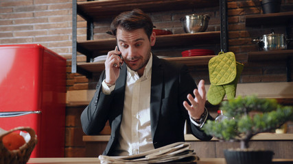 Good looking young man in formal wear sitting at home and talking on the phone, actively...