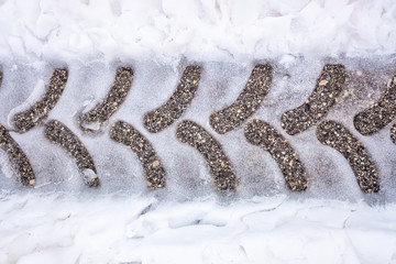Traces of a tractor tire on snowy asphalt on a road in winter.