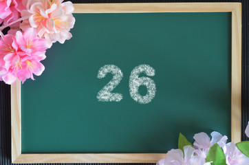 Number 26 write with white chalk, flowers on the board.