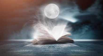 An open book on a wooden table under the night sky against a dark forest. Magical radiance. Night...