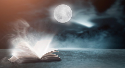 An open book on a wooden table under the night sky against a dark forest. Magical radiance. Night...