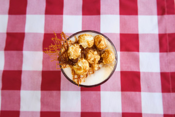 Glass of coffee latte with whipped cream, caramel popcorn, cinnamon and salty caramel on table, top view