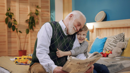 Happy grandfather and grandson while reading book sitting at home generation book happiness child reading kid man caucasian family happy childhood grandchild slow motion