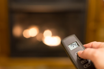 Gas log fireplace being turned on with a remote control that shows the temperature of the room.