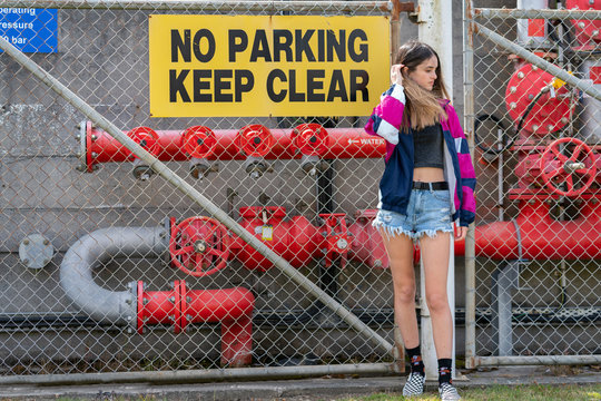 Young woman standing in front of  hurricane chain link fence and industrial gas piping