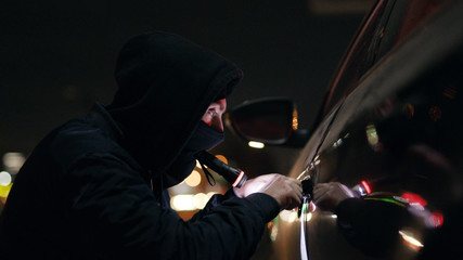 Quickly robber checking breaking entering alarm shines a flashlight in a car sitting stealing crime male thief illegal theft stolen danger burglary bandit secure safety money insurance door - obrazy, fototapety, plakaty