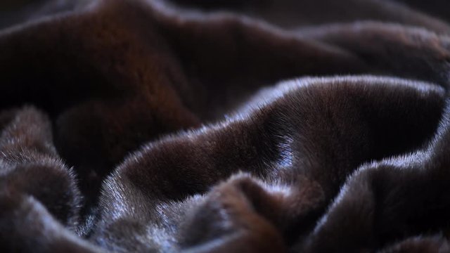 Mink Fur background. High quality Canadian black Fur clothes texture closeup. Soft and fluffy dark brown mink Texture surface Rotation. Slow motion. Macro shot. 4K UHD video
