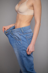 Woman Shows her Weight Loss and Wearing Her Old Jeans. Slim Girl in Big Jeans Showing How She Was Losing Weight When She Started Eating Healthy Food.