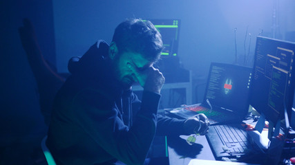 Profile of stressed hacker trying a virus attack on corporate servers in dark place. Night hacking...