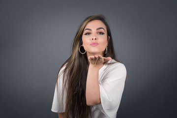 Cute appealing female blows kiss at camera, demonstrates love to boyfriend or says goodbye on distance, isolated over white studio background. Attractive young woman shows sympathy to someone.