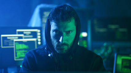 Portrait of menacing serious computer hacker working with codes on laptop at desk. Cyber crime and...