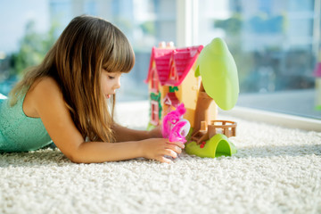 Adorable little girl playing with a dollhouse while sitting on the floor