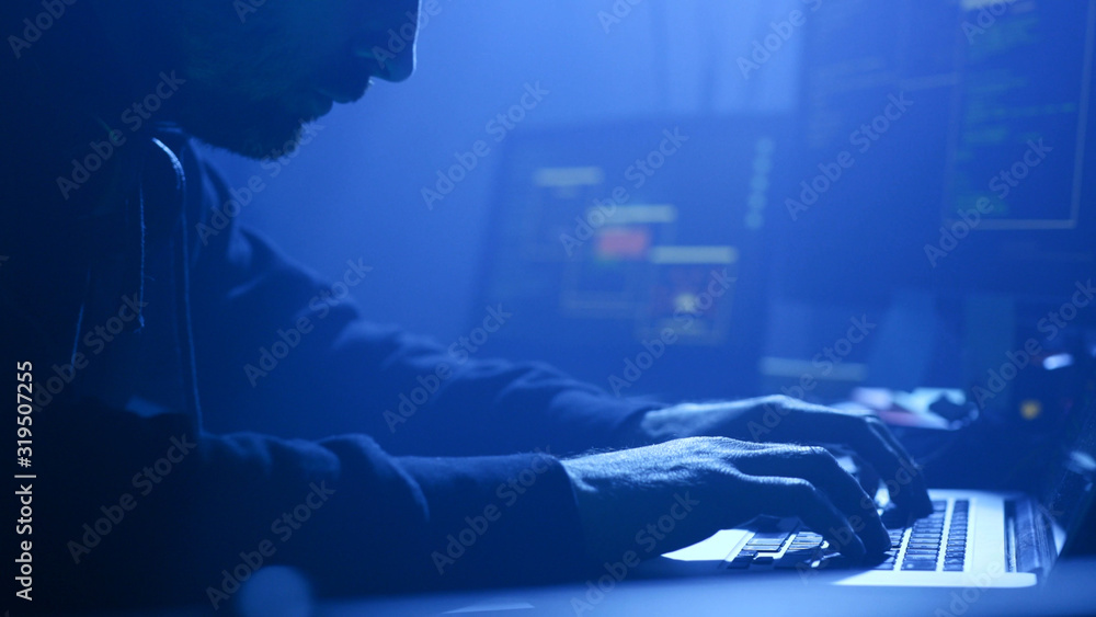 Poster close-up of professional computer hacker writing data codes typing on laptop at night in the office.
