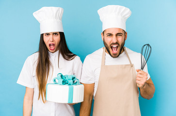 Young couple cooking a cake together isolated screaming very angry and aggressive.