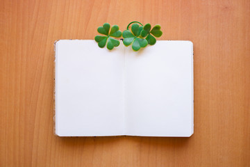 Open and blank notebook with three and four-leaf clovers on top.