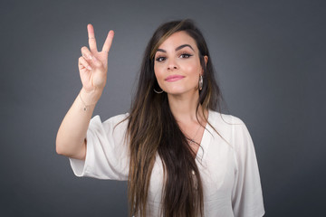 Young middle aged caucasian woman standing against gray wall showing and pointing up with fingers number two while smiling confident and happy.