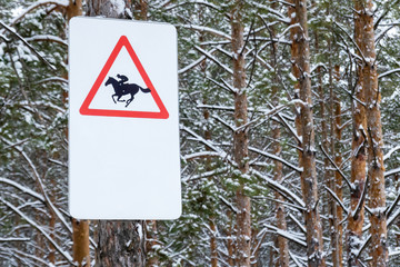 Winter forest. On the tree hangs a pointer with the image of a sports horse in a red triangle....