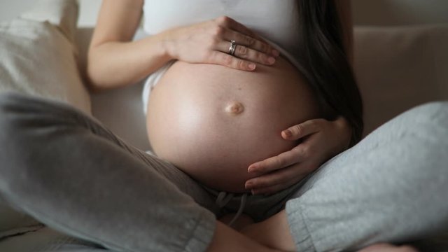 Close-up of the pregnant woman's belly while she's stroking and touching it with her hand at home. Slow motion video
