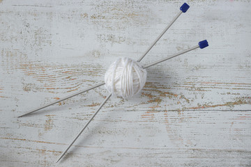 White skein of yarn and knitting needles on a wooden background. Top view.
