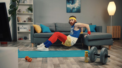 Handsome silly sportsman doing exercise leaning on a sofa watching fitness videos at home.