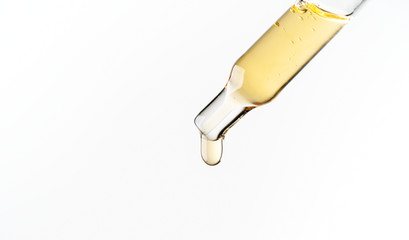 Cosmetic pipette with a liquid drop dripping close up on white background. Macro view transparent...