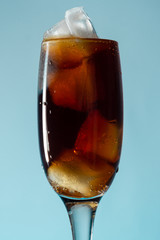 Glass goblet with brown soda and ice blue background, close up, copy space
