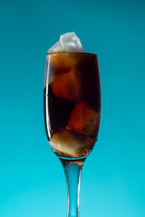 Glass goblet with brown soda and ice blue background, close up, copy space