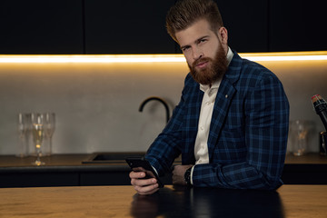 Handsome stylish man in blue suit in cage at home. Sitting in modern black kitchen with smart phone in hand.