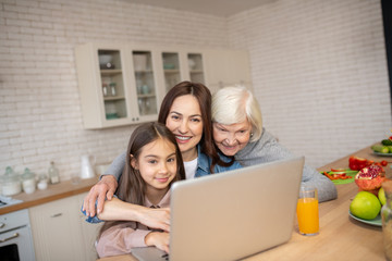 Grandmother, mother, daughter hugged at a laptop in the kitchen.