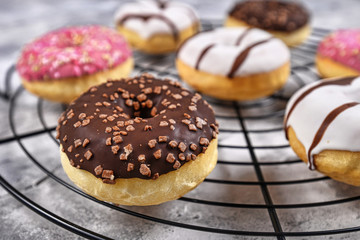 Tasty baked donut with brown chocolate glazing and sprinkles on cake grid with other colorful donuts in background