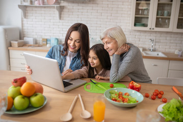 Mom daughter grandmother watching online recipes in a laptop.