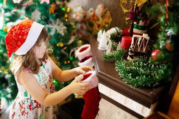 Little girl searching for candy and gifts in advent calendar (Xmas socks) on winter morning. Kid opening Christmas presents.