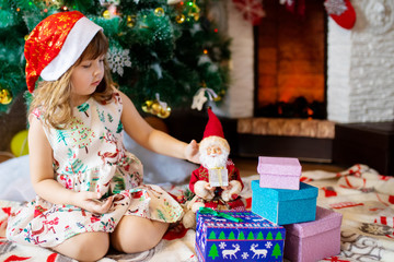 Fototapeta na wymiar Adorable little girl opening her christmas presents beside a christmas tree. Happy kid standing with of christmas gift boxes