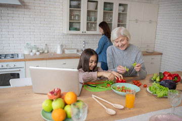 Grandmother and granddaughter cooking fresh vegetable salad.